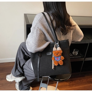 Detail of black tote bag with cute brown teddy bear charm and sleek shoulder strap