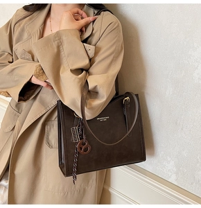 Detail of deep brown frosted leather tote bag with gold logo and stylish charm on model