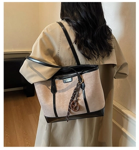 Detail of beige suede tote bag with black glossy straps worn by model in a chic indoor setting