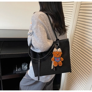 Minimalist black tote bag with cute teddy bear charm shown in a cozy indoor lifestyle scene