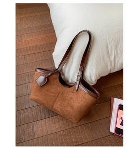 Detailed close-up of brown suede tote bag with leather piping on a white pillow background