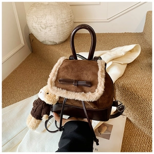 Detail of a brown leather backpack with plush trim, bow decoration, and a bear charm