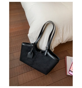 Detail of a black matte tote bag with leather trim on a wooden floor by a white pillow