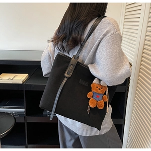 Detail view of black tote bag in matte texture with cute decorative plush bear charm