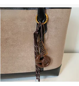 Detail of beige suede tote bag with black leather trim and decorative gold abacus charm