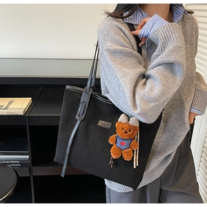 Detail of black matte tote bag featuring a cute brown plush bear charm and leather strap