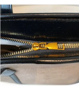 Detail of smooth gold zipper and black leather trim on a beige tote bag