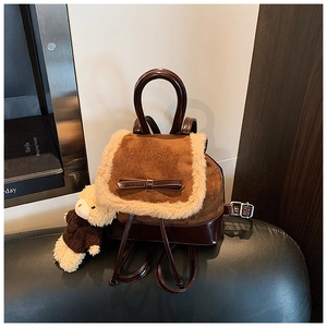 Detail of mini backpack with teddy bear charm and bow decoration on dark leather
