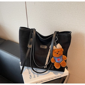 Detail of black matte tote bag with silver plaque on a book with cute bear charm