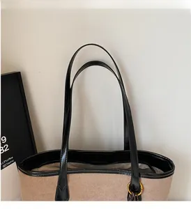 Detail of khaki suede tote bag showing sturdy black handles and silver logo plaque