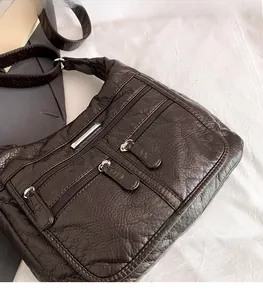 Detail of dark brown soft leather crossbody bag with multiple zippers and pleated texture