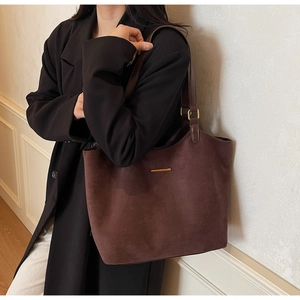Detail van een donkere matte leren shopper met gouden accenten gedragen door een model