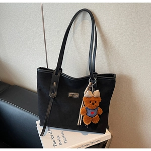 Detail of black matte tote bag featuring a cute plush bear charm and metallic brand plaque