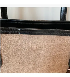 Detail of a brown suede tote bag with black leather trim and golden logo engraving