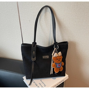 Detail of black matte tote bag with metal logo and cute plush bear charm accessory