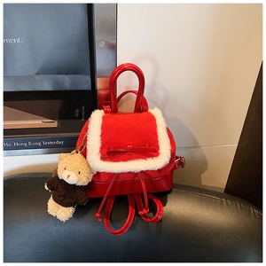 Detail of red mini backpack featuring white plush trim, a bow, and a teddy bear charm