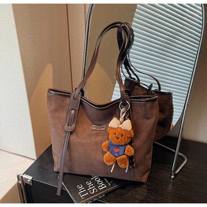 Detail of dark brown suede tote bag with a cute teddy bear charm and leather strap