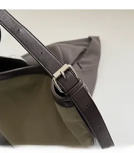 Detail of silver square buckle and adjustable brown leather strap on green canvas bag
