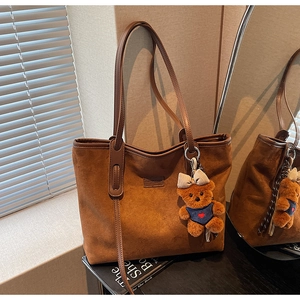 Detailed close-up of brown suede tote bag with leather handles and cute bear charm