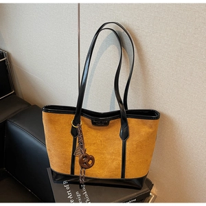 Dettaglio borsa tote in pelle scamosciata caramello con finiture in pelle nera e ciondolo
