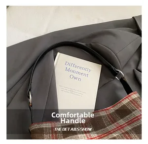 Detail of comfortable leather handle on a red-brown plaid crossbody bag with silver rings
