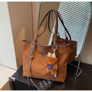 Detailed view of brown suede tote bag featuring fashion label and cute bear charm