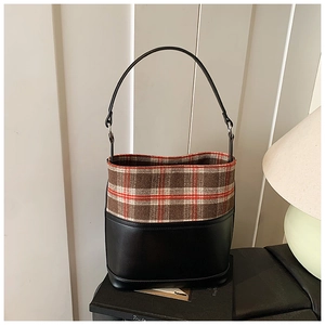 Detail of the chic bucket bag featuring black leather and red brown plaid fabric textures