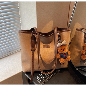 Detail of retro brown suede tote bag with leather piping and cute teddy bear charm