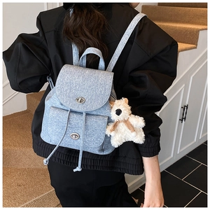 Detail eines hellblauen Denim-Rucksacks mit Metalldrehverschlüssen und Bärenanhänger
