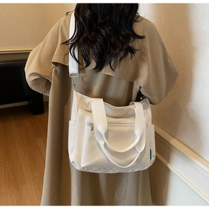 Détail d'un sac cabas blanc en nylon montrant les poches zippées et la bandoulière réglable