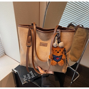 Detailed view of large brown suede tote bag with leather trim and cute bear charm accent
