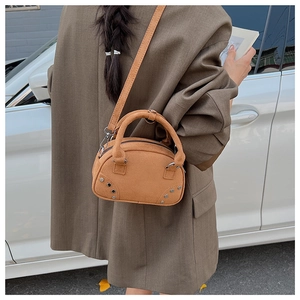 Detailed view of camel suede bowling bag with rivet accents in a street style setting