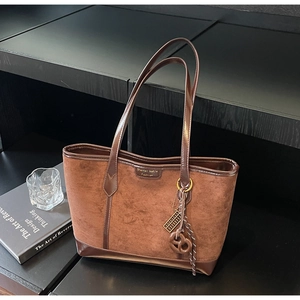 Dettaglio di una borsa tote marrone in pelle scamosciata con ciondolo retrò