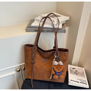 Close-up of brown suede tote bag with leather logo label and cute teddy bear charm