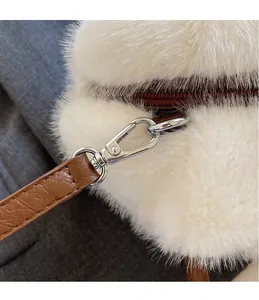 Detailaufnahme des silbernen Metallhakens und Lederriemens an weißer Plüsch-Handtasche