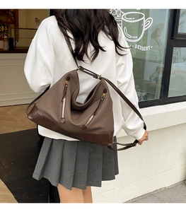 Detailed view of brown leather bucket bag with gold zippers and reinforced dark base