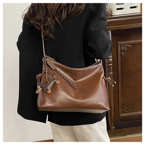 Detail view of brown leather hobo bag featuring a dachshund charm and woven rope accent
