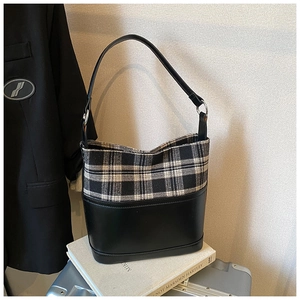 Detail of checkered bucket bag resting on books and silver luggage for a commute look