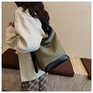 Detail of army green canvas bucket bag with brown leather trim and black strap on model