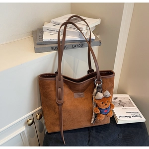 Detail of brown matte tote bag with teddy bear charm on textured cushion background