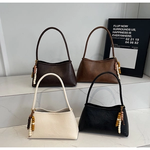 Detail view of four minimalist faux leather shoulder bags in various colors on marble display