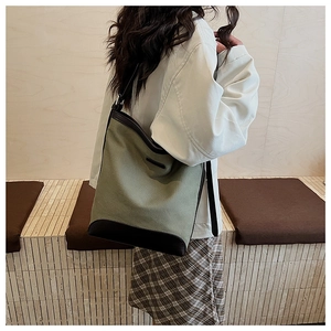Detail of olive green canvas tote with black leather trim worn on the shoulder