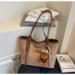 Detail view of brown matte tote bag with leather straps and a cute plush bear charm