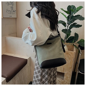 Side view of large green canvas tote bag with black leather trim on a female model