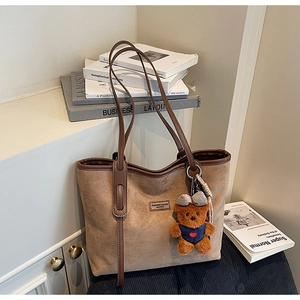 Detail view of khaki suede tote bag with leather straps and a cute teddy bear charm