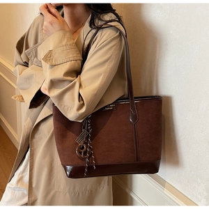 Dettaglio di una borsa tote marrone con placca in metallo e ciondolo in corda intrecciata