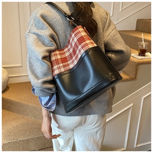Detail view of stylish checkered bucket bag worn by model, showing leather and fabric mix