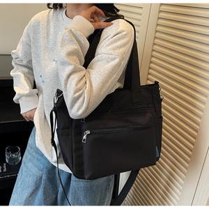 Détail d'un sac cabas en nylon noir avec plusieurs poches zippées et doubles bandoulières