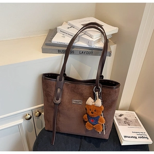 Close-up of brown suede tote bag with a cute bear plush keychain and leather straps
