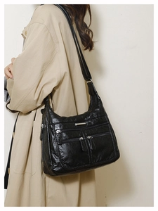 Detail of black soft leather crossbody bag featuring triple zipper pockets on a model